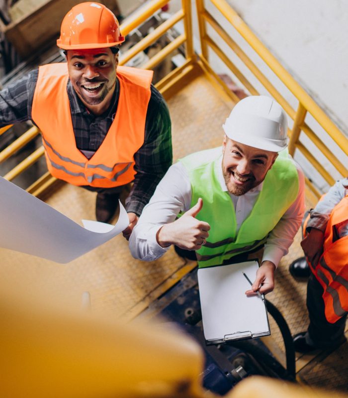 Three factory workers in safety hats discussing manufacture plan